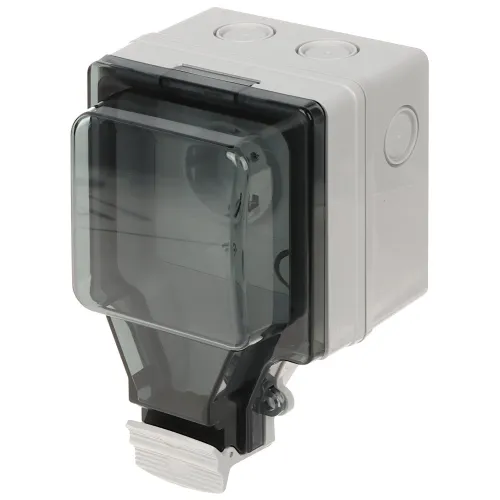 Na zdjęciu znajduje się szara, plastikowa obudowa elektryczna z przezroczystą, ciemną pokrywą. Obudowa ma prostokątny kształt i jest wyposażona w otwory montażowe na górze.