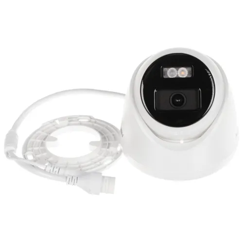Na zdjęciu znajduje się biała kamera monitoringu z czarnym panelem frontowym, wyposażona w dwa diody LED i obiektyw. Obok kamery leży biały kabel z okrągłym mocowaniem.