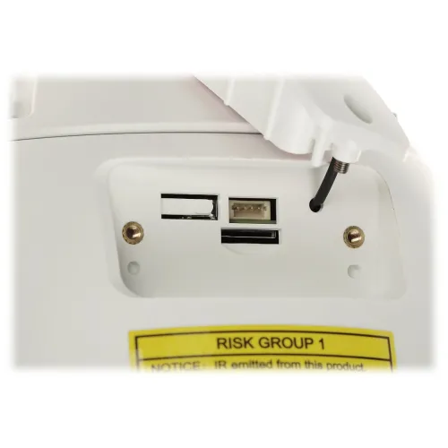 Zdjęcie przedstawia zbliżenie na panel urządzenia z gniazdem na kartę pamięci, portem USB oraz przyciskiem reset. W dolnej części widoczna jest żółta naklejka z ostrzeżeniem "RISK GROUP 1".