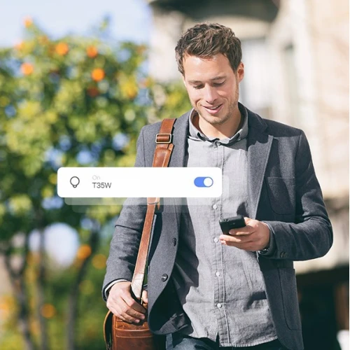 Mężczyzna w szarym garniturze i z brązową torbą na ramieniu patrzy na telefon, stojąc na zewnątrz. Na zdjęciu widoczna jest również grafika przedstawiająca włączony przełącznik Wi-Fi z napisem "T35W".