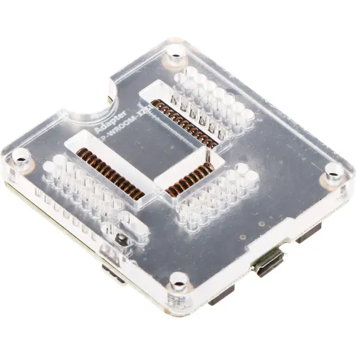 Przezroczysty adapter elektroniczny z widocznymi złączami i pinami, umieszczony na białym tle. Adapter ma prostokątny kształt z zaokrąglonymi narożnikami i metalowymi elementami wewnątrz.